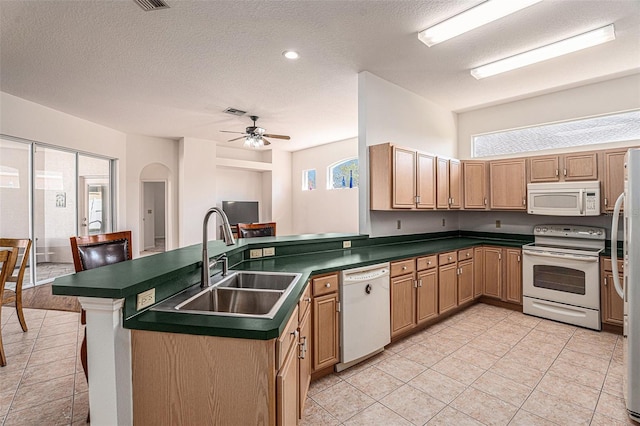 kitchen featuring a peninsula, white appliances, a sink, a ceiling fan, and dark countertops