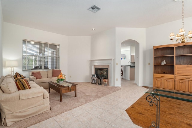 living room featuring arched walkways, light tile patterned flooring, light colored carpet, visible vents, and a tiled fireplace