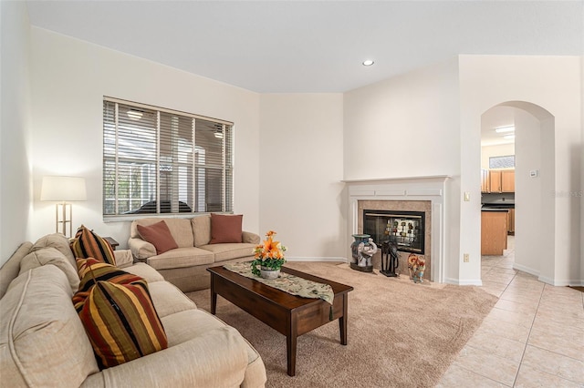 living area featuring arched walkways, light tile patterned flooring, light colored carpet, a fireplace, and baseboards