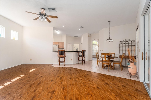 living room featuring light wood-style flooring, visible vents, ceiling fan, and baseboards