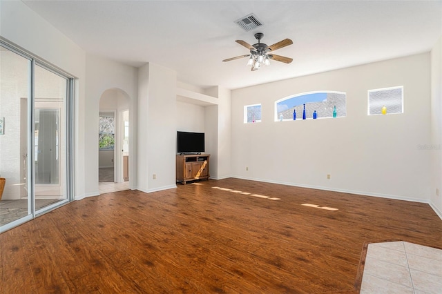 unfurnished living room with a healthy amount of sunlight, visible vents, arched walkways, and wood finished floors