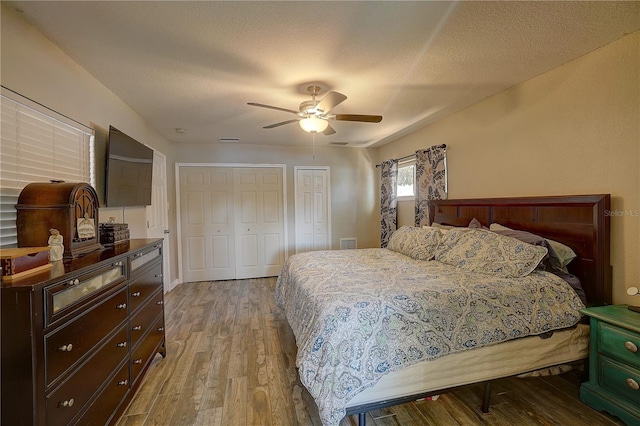 bedroom with multiple closets, ceiling fan, a textured ceiling, and wood finished floors