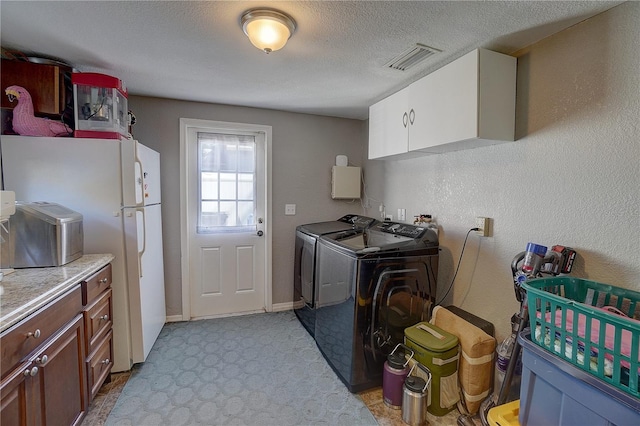 laundry area featuring cabinet space, visible vents, a textured wall, washing machine and clothes dryer, and a textured ceiling