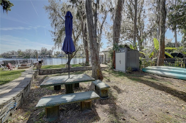 exterior space with a water view, an outdoor fire pit, fence, a shed, and an outdoor structure