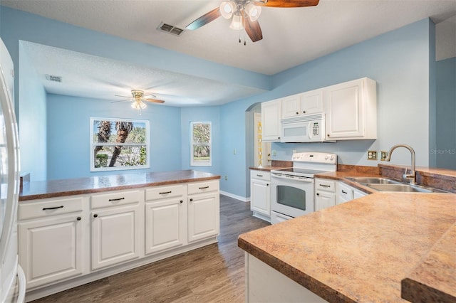 kitchen with a peninsula, white appliances, a sink, visible vents, and white cabinets