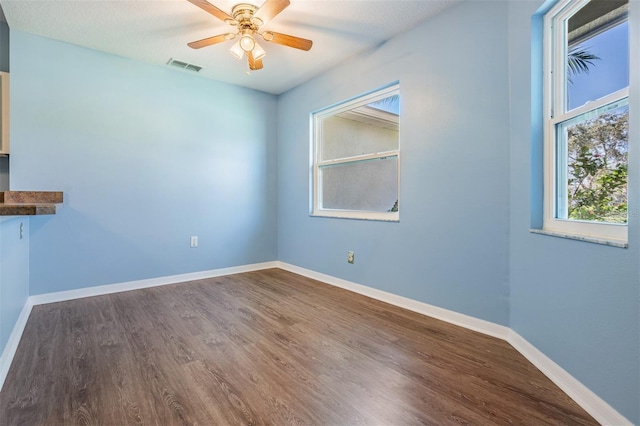 spare room featuring a ceiling fan, visible vents, baseboards, and dark wood-type flooring