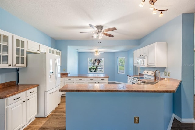 kitchen with a peninsula, white appliances, white cabinetry, and glass insert cabinets