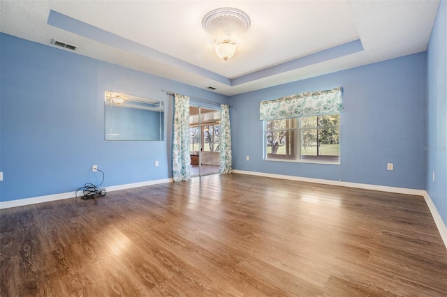 spare room with a raised ceiling, visible vents, baseboards, and wood finished floors