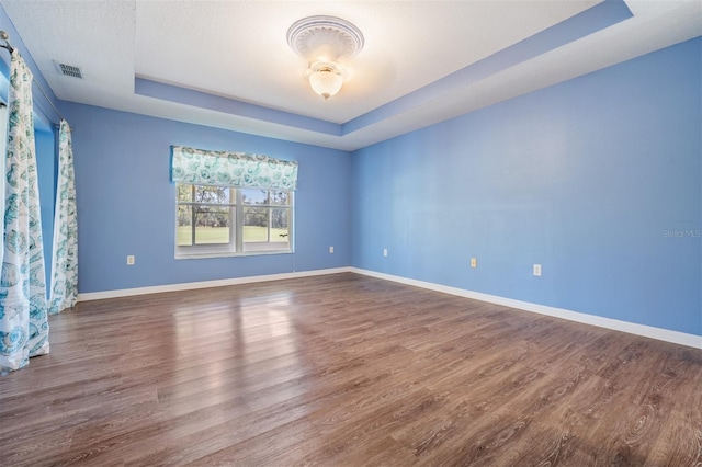 unfurnished room with a raised ceiling, visible vents, baseboards, and wood finished floors