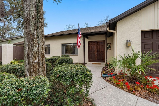 entrance to property with a shingled roof, fence, and stucco siding