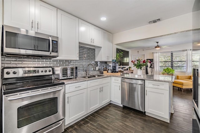 kitchen featuring a peninsula, appliances with stainless steel finishes, a sink, and white cabinets