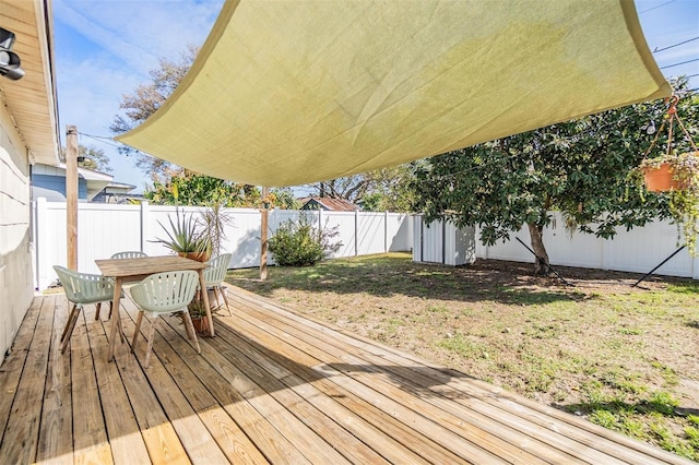 wooden terrace featuring outdoor dining area, a fenced backyard, and a lawn