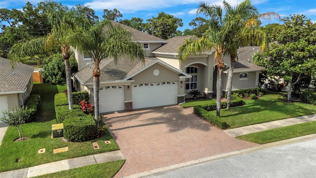 view of front of home with a garage, roof with shingles, decorative driveway, stucco siding, and a front lawn