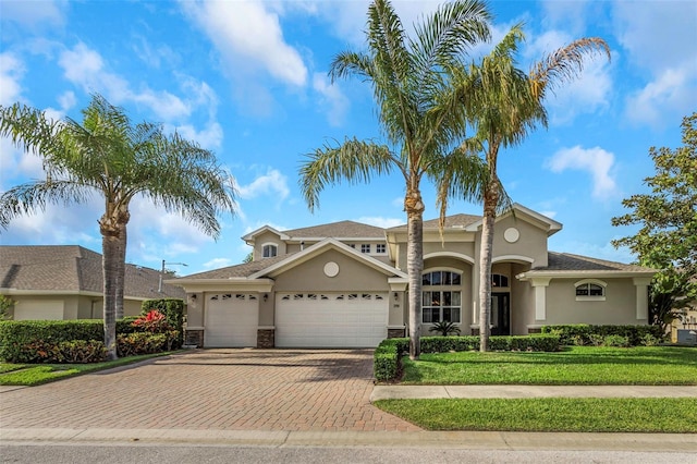 mediterranean / spanish home featuring a garage, a front yard, decorative driveway, and stucco siding