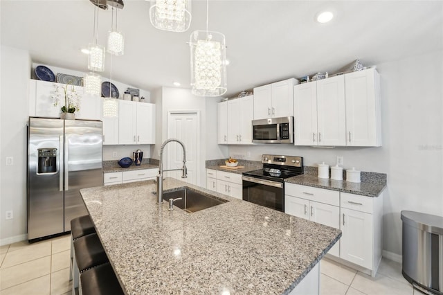 kitchen featuring an island with sink, appliances with stainless steel finishes, white cabinetry, pendant lighting, and a sink