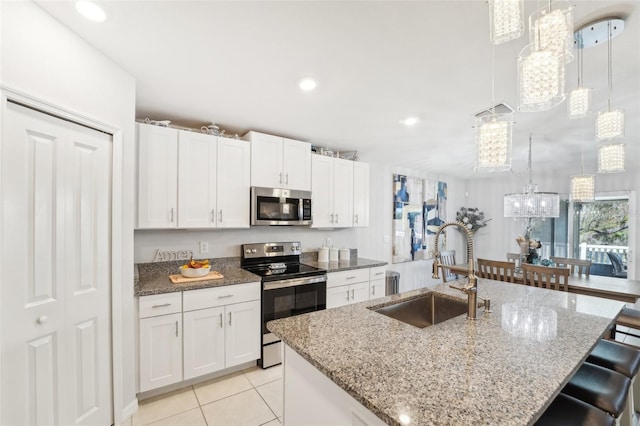 kitchen with stainless steel appliances, hanging light fixtures, white cabinets, a sink, and an island with sink