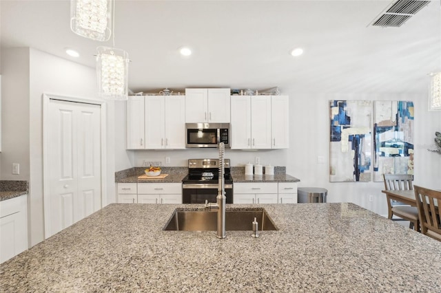 kitchen featuring white cabinetry, visible vents, appliances with stainless steel finishes, dark stone countertops, and decorative light fixtures