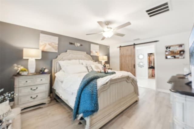 bedroom with ceiling fan, a barn door, light wood-style flooring, visible vents, and a spacious closet