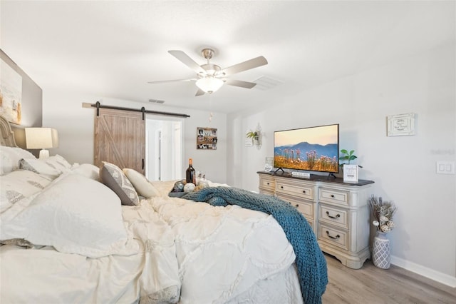 bedroom featuring a barn door, visible vents, baseboards, a ceiling fan, and light wood-style floors