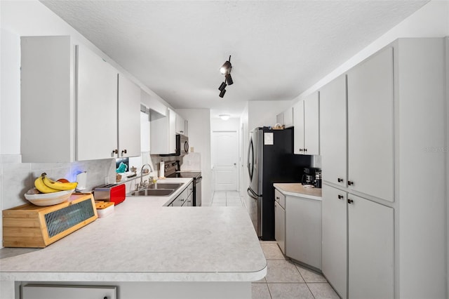 kitchen featuring light tile patterned floors, stainless steel appliances, a peninsula, a sink, and light countertops