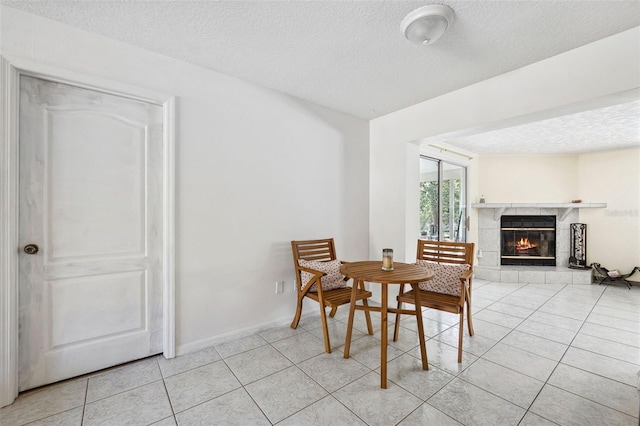 dining area featuring light tile patterned floors, a textured ceiling, a tiled fireplace, and baseboards