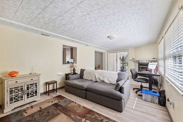 living room featuring baseboards, visible vents, wood finished floors, and a glass covered fireplace