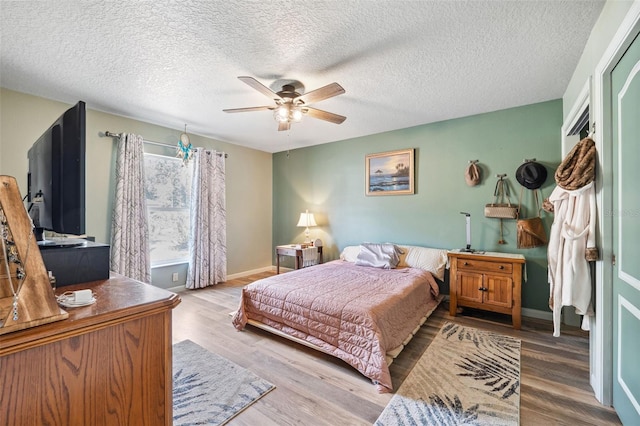 bedroom featuring a ceiling fan, a textured ceiling, baseboards, and wood finished floors