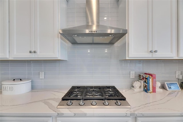 kitchen with white cabinets, decorative backsplash, light stone counters, wall chimney range hood, and stainless steel gas cooktop