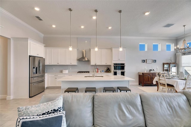 kitchen with stainless steel appliances, wall chimney exhaust hood, a sink, and visible vents