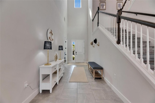 foyer entrance with stairs, a high ceiling, light tile patterned flooring, and baseboards