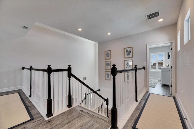 hallway featuring visible vents, wood finished floors, an upstairs landing, and baseboards