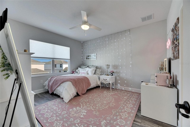 bedroom with a ceiling fan, visible vents, baseboards, and wood finished floors