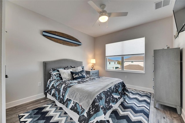 bedroom with a ceiling fan, visible vents, baseboards, and wood finished floors