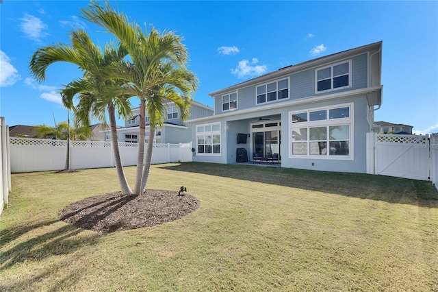 rear view of house featuring a lawn, a fenced backyard, and a gate