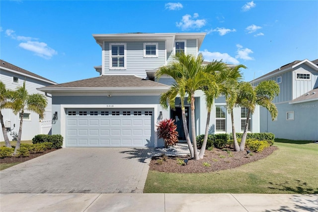 view of front facade featuring an attached garage, a front yard, decorative driveway, and roof with shingles