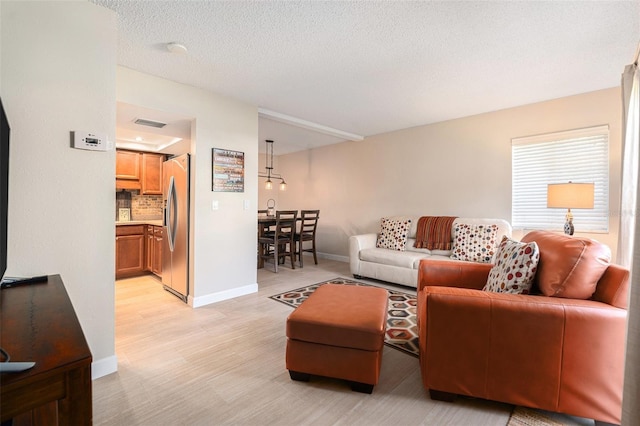 living room featuring light wood-style floors, visible vents, baseboards, and a textured ceiling