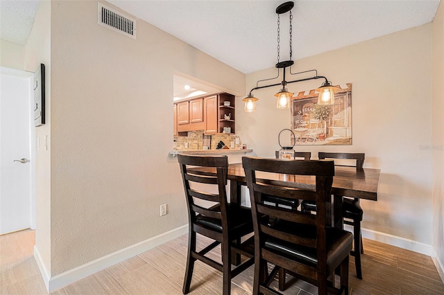 dining area featuring visible vents, a textured ceiling, baseboards, and wood finished floors