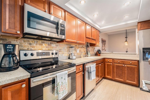 kitchen featuring a tray ceiling, brown cabinets, stainless steel appliances, tasteful backsplash, and a sink