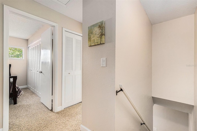 hallway featuring light carpet, baseboards, a textured ceiling, and an upstairs landing