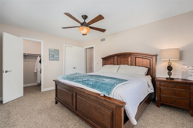 bedroom featuring light carpet, visible vents, baseboards, ceiling fan, and a walk in closet