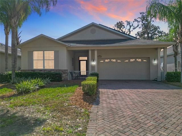 single story home with stone siding, decorative driveway, an attached garage, and stucco siding