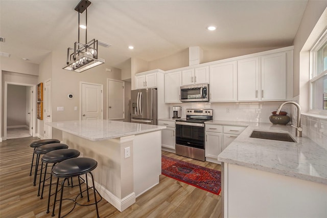 kitchen featuring stainless steel appliances, a sink, a kitchen island, white cabinetry, and hanging light fixtures