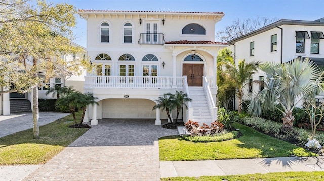 mediterranean / spanish home featuring a balcony, stairway, an attached garage, decorative driveway, and french doors