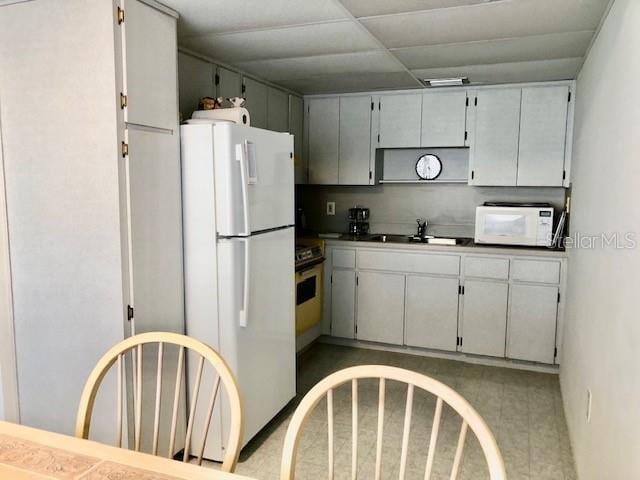 kitchen featuring dark countertops, white appliances, a drop ceiling, and a sink