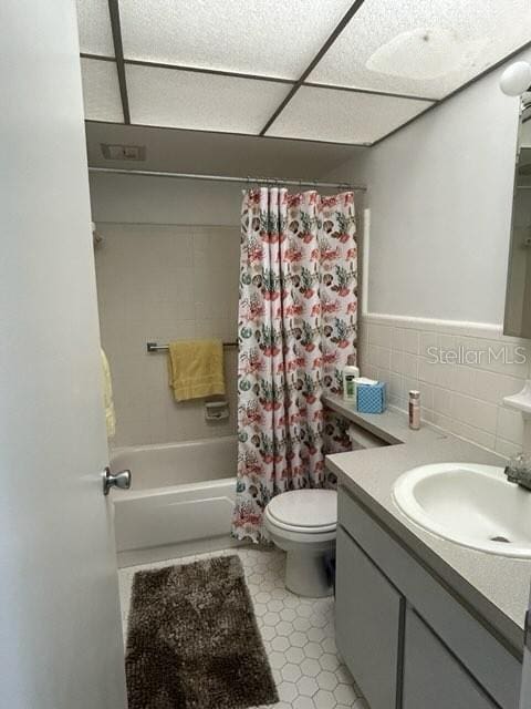 full bathroom featuring toilet, a wainscoted wall, shower / bath combo with shower curtain, vanity, and tile walls