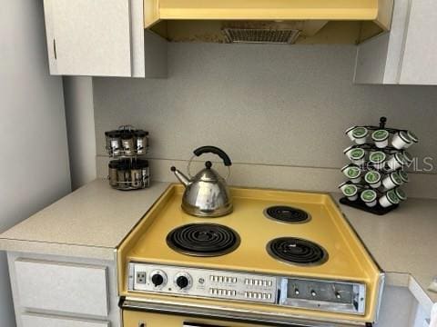 kitchen featuring light countertops, cooktop, white cabinetry, and under cabinet range hood