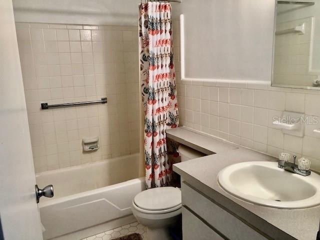 bathroom with shower / tub combo, toilet, tile patterned floors, vanity, and tile walls