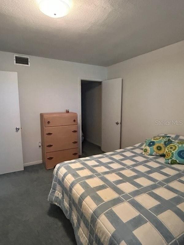 bedroom with a textured ceiling, dark carpet, and visible vents