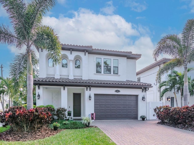 mediterranean / spanish-style home with an attached garage, stucco siding, decorative driveway, and a tiled roof