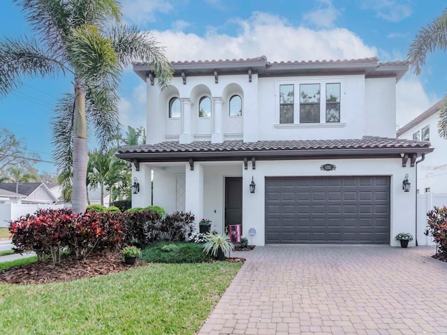 mediterranean / spanish-style home with a garage, a tiled roof, decorative driveway, and stucco siding